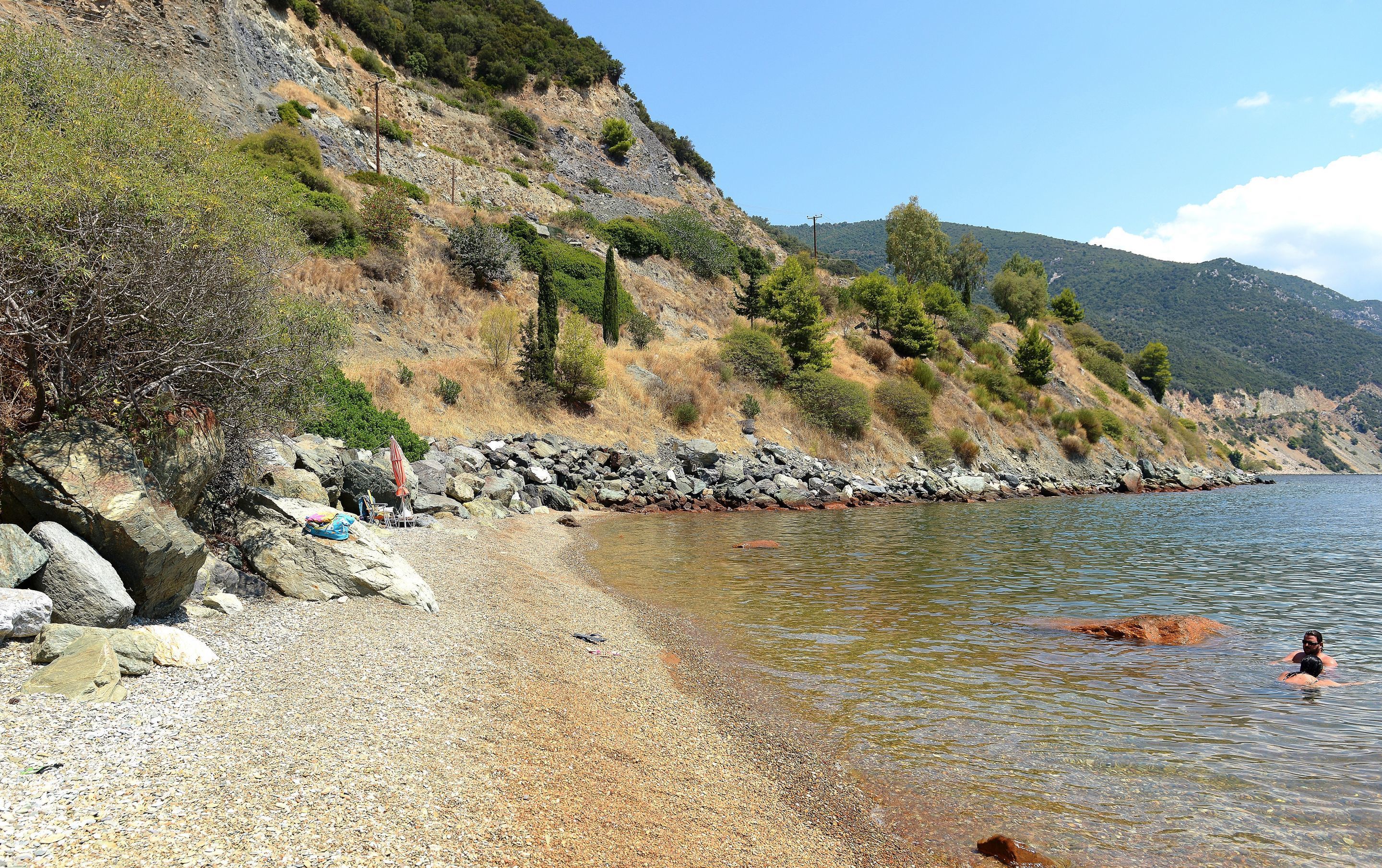 Ein felsiger Strand mit freiem Blick auf das Wasser und einer hügeligen Landschaft im Hintergrund.