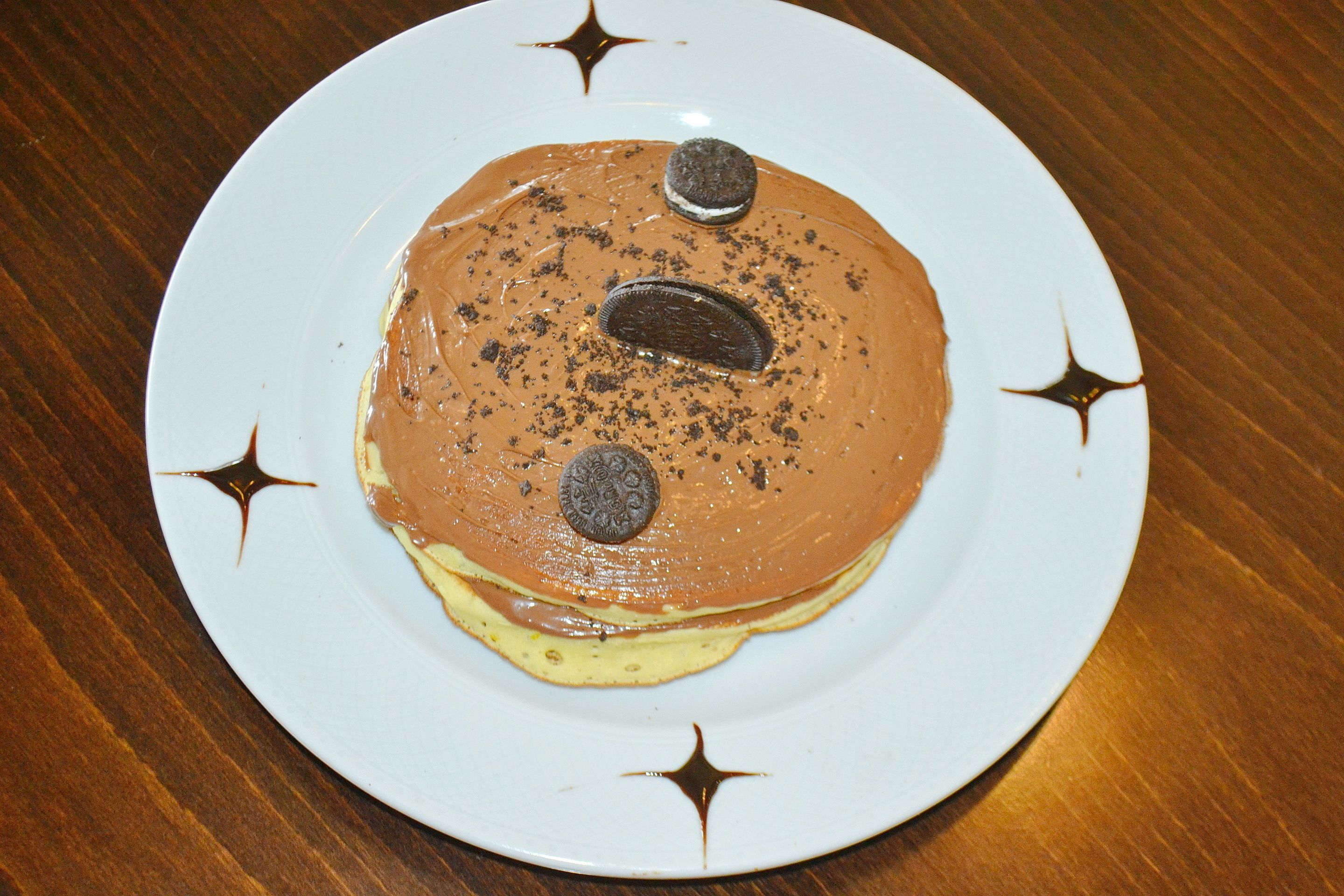 A plate with a layered dessert, including a chocolate spread, cookies, and a yellow base, on a white plate with star designs.