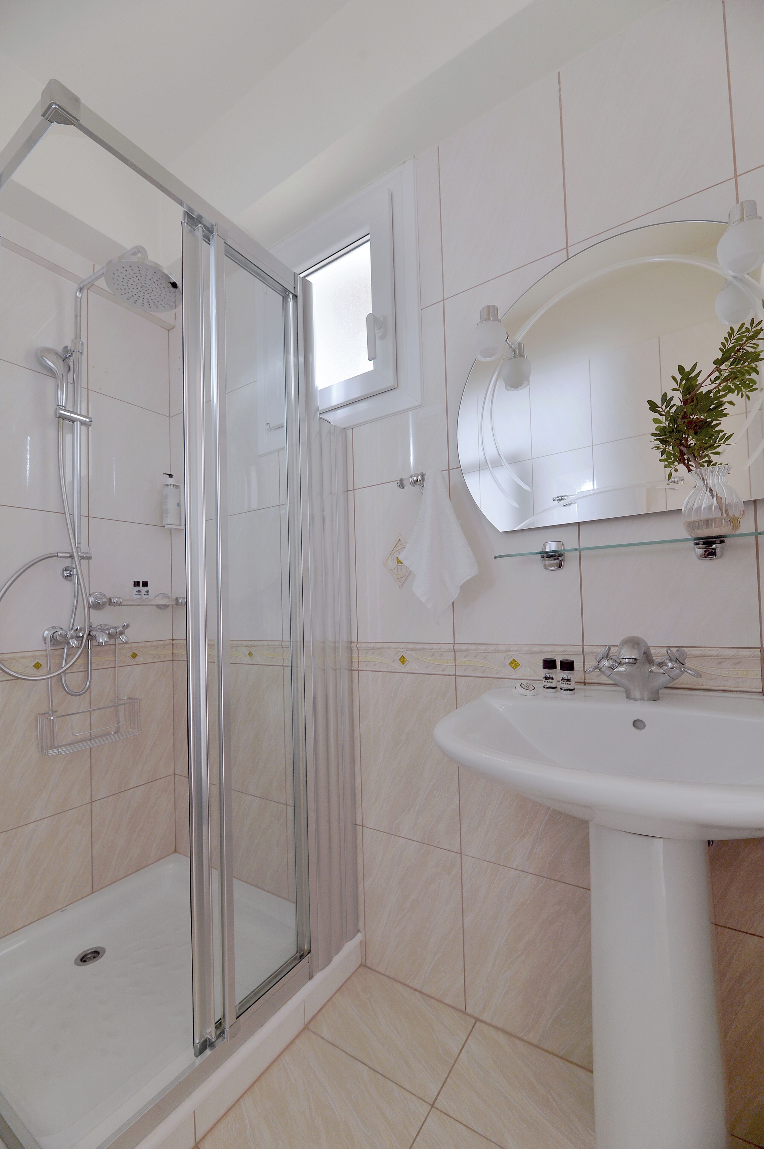Un baño con cabina de ducha de vidrio, un lavabo blanco y un espejo sobre él.