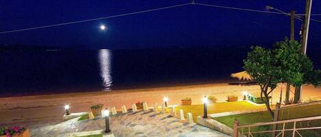 A nighttime view of a beachside walkway with stone steps and potted plants, leading to a grassy area with a view of the ocean.