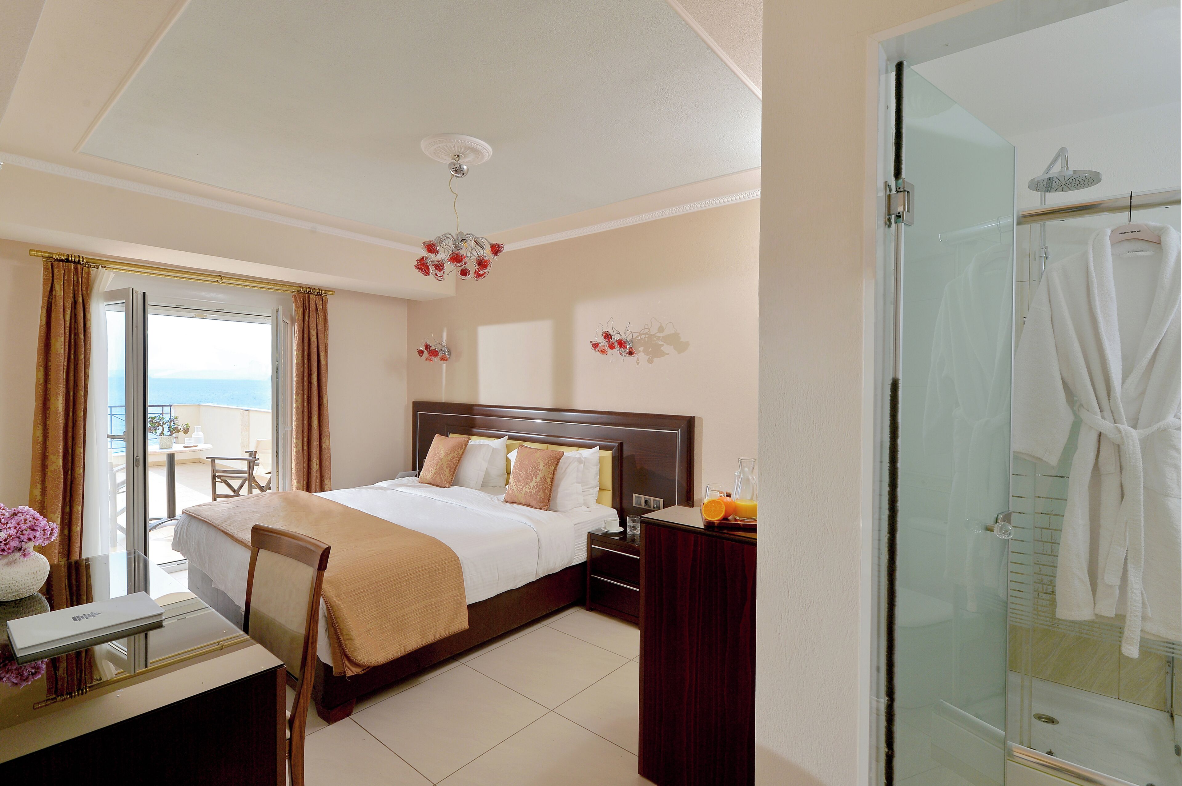 Une chambre d’hôtel équipée d’un lit, d’un bureau, d’une chaise, d’une douche en verre et offrant une vue sur la mer.