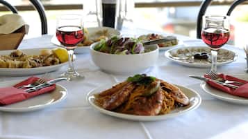 Une table dressée avec divers plats, notamment des pâtes et des fruits de mer, ainsi que deux verres de vin rouge.