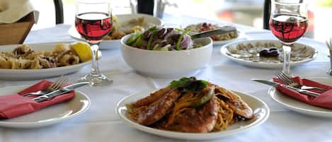 A table set with various dishes, including pasta and seafood, and two glasses of red wine.