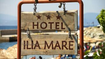 A wooden sign with "HOTEL" and "ILIA MARE" written on it, hanging from a metal frame.