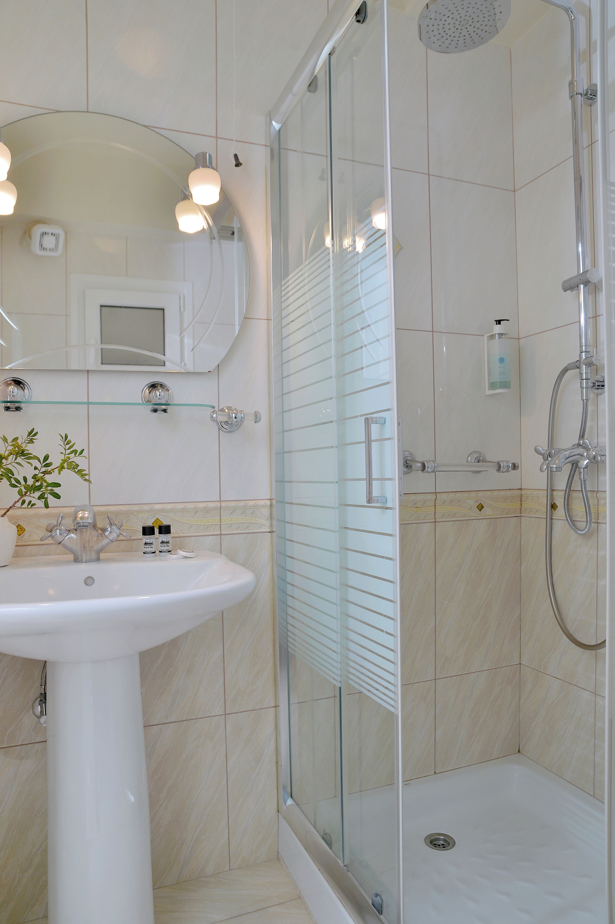 A bathroom with a glass-enclosed shower, a pedestal sink, and a mirror with lights.