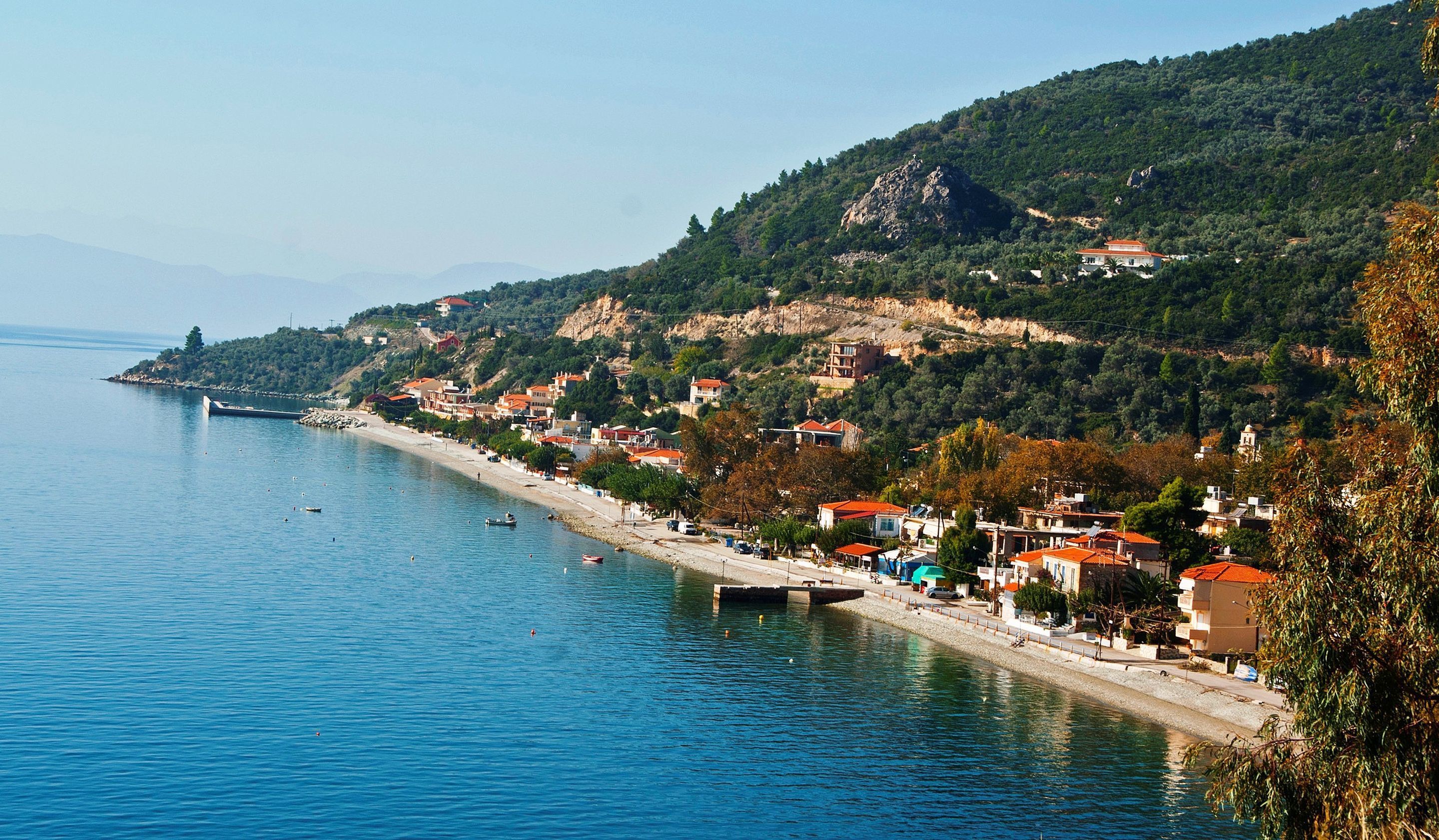 A coastal town with a beach, houses with red roofs, and a rocky hillside.