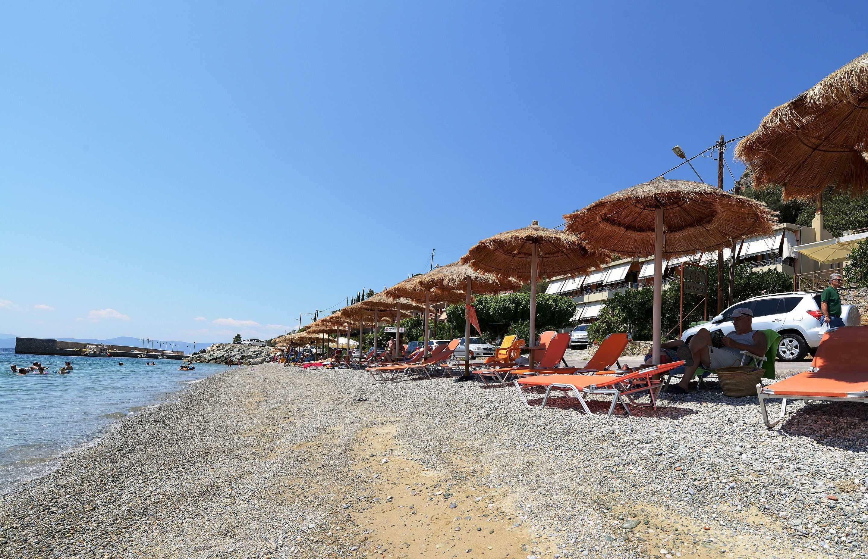 A pebbled beach with rows of orange lounge chairs and thatched umbrellas.