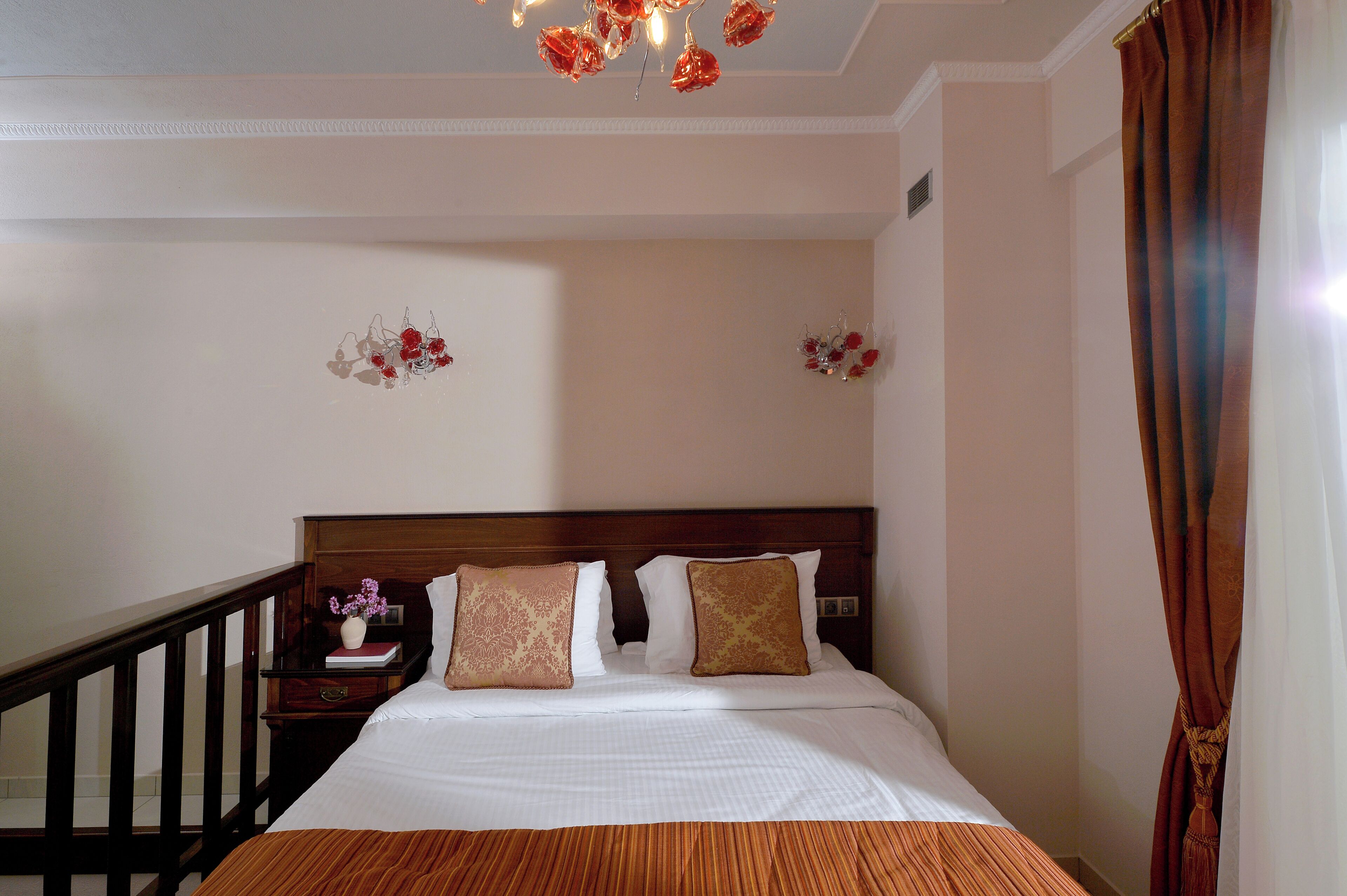 A hotel room with a bed, wooden headboard, a nightstand with a vase of flowers, and a staircase.