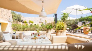 Un espace extérieur aménagé pour les repas, avec des tables et des chaises, entouré de plantes en pot et de parasols.