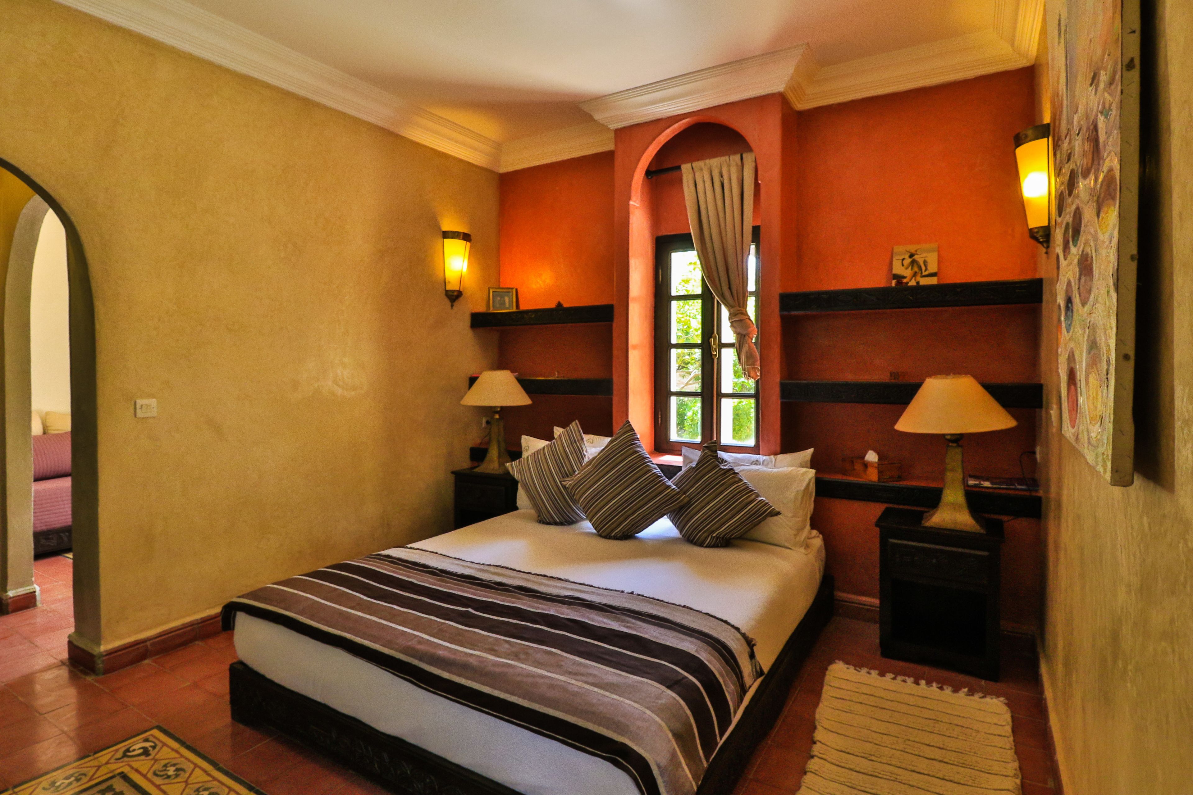 A hotel room with a large bed, two bedside tables with lamps, a window with curtains, and a decorative wall with a picture.