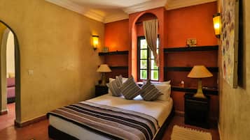 A hotel room with a large bed, two bedside tables with lamps, a window with curtains, and a decorative wall with a picture.