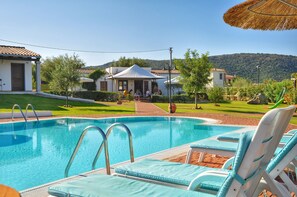 Una piscina con sillas de descanso, un área de estar cubierta y vistas del paisaje circundante.