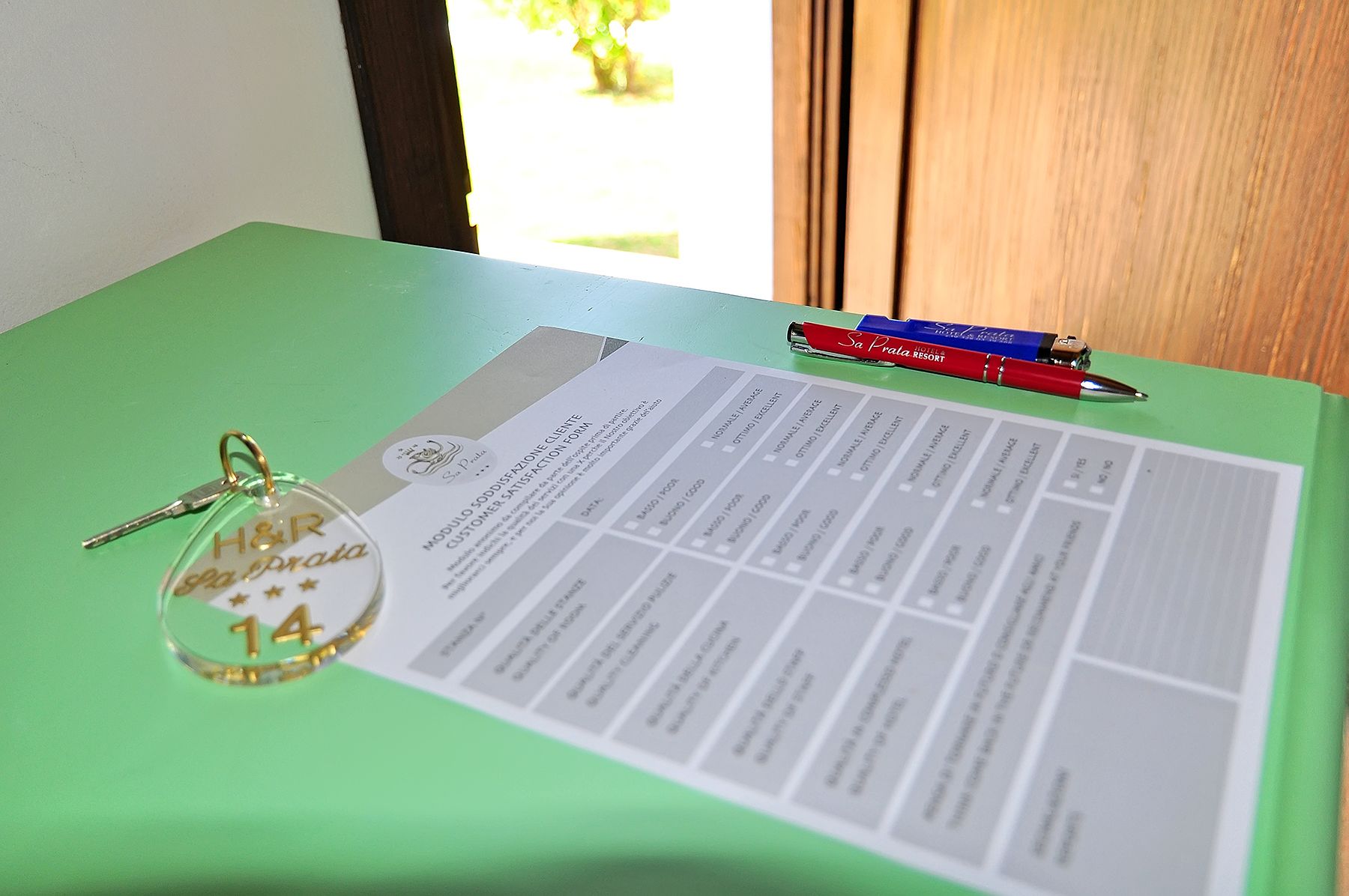A hotel keychain with "H&L" and a number 14, a customer satisfaction form, and a pen on a green table.