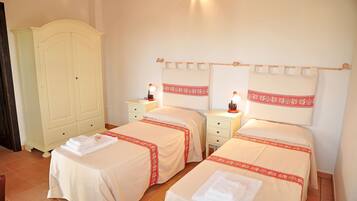 Habitación de hotel con dos camas, cada una con una colcha estampada en rojo y blanco, una mesita de noche con lámpara y un armario.