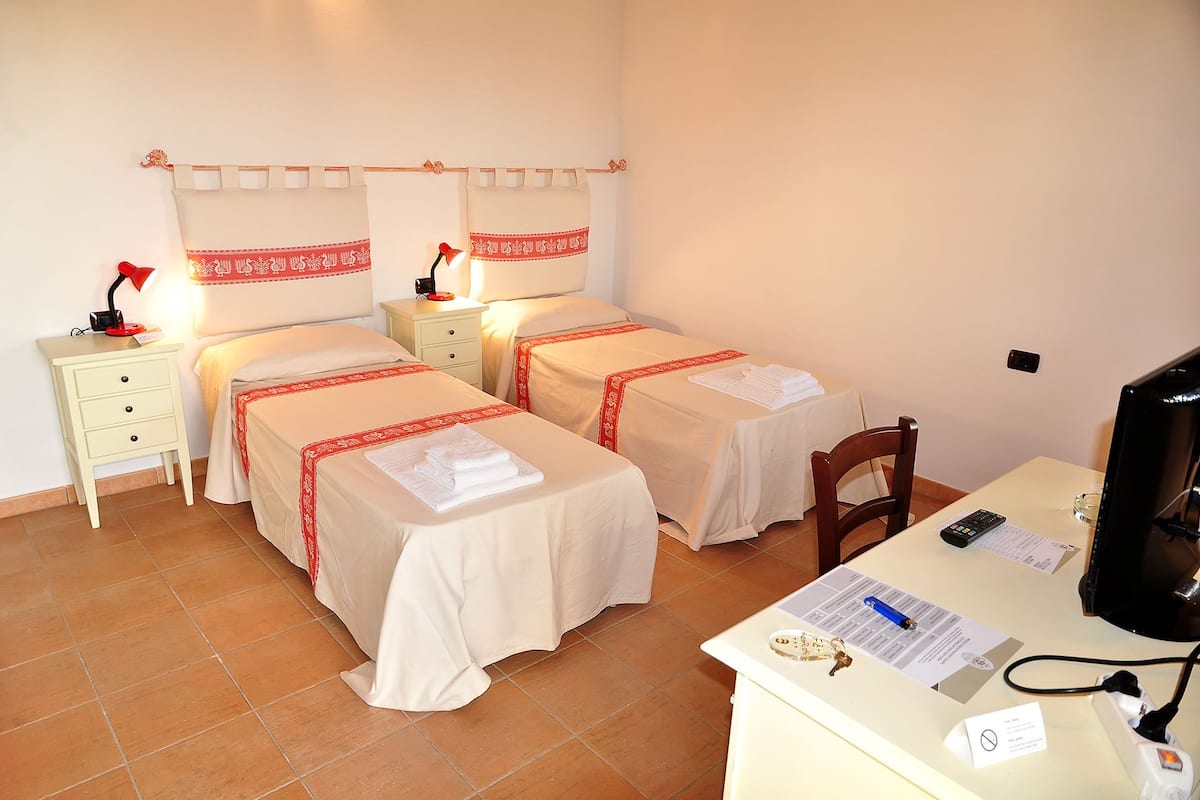 A hotel room with two beds, each with a red and white bedspread, a desk with a computer, and a chair.