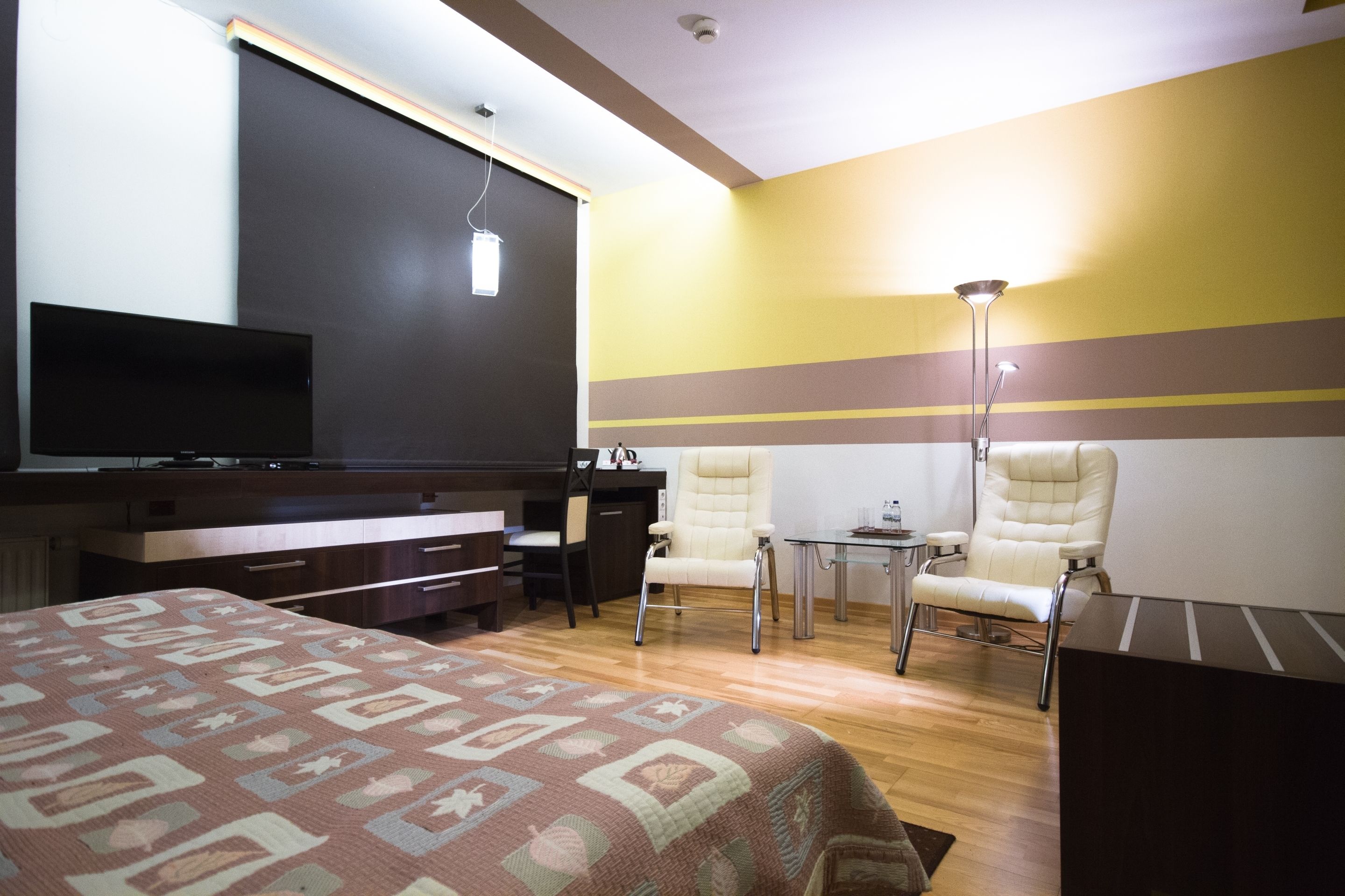 Una habitación de hotel con cama, escritorio, dos sillas, televisión y lámpara.