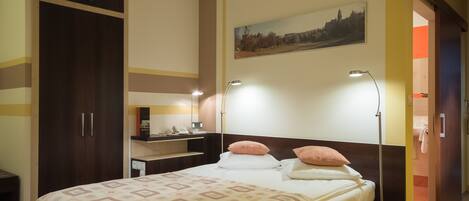 Habitación de hotel con cama, lámparas de noche, armario, escritorio y un cuadro en la pared.