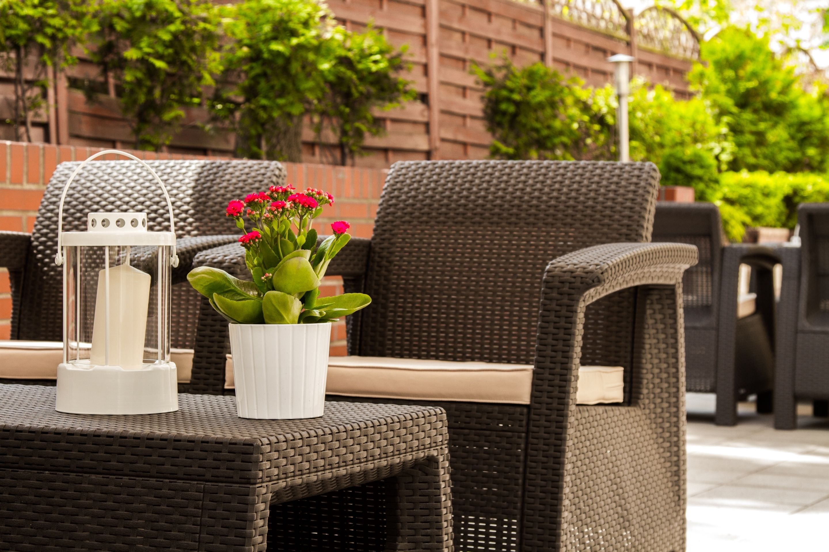 An outdoor seating area with wicker furniture, a white lantern, and a potted plant with red flowers.