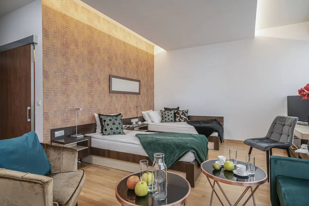 Quarto de hotel moderno com cama, mesas de cabeceira, escrivaninha e área de estar.