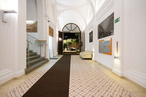 Et hotellets reception område med et tæppe og en skranke, samt en trappe til en anden etage.