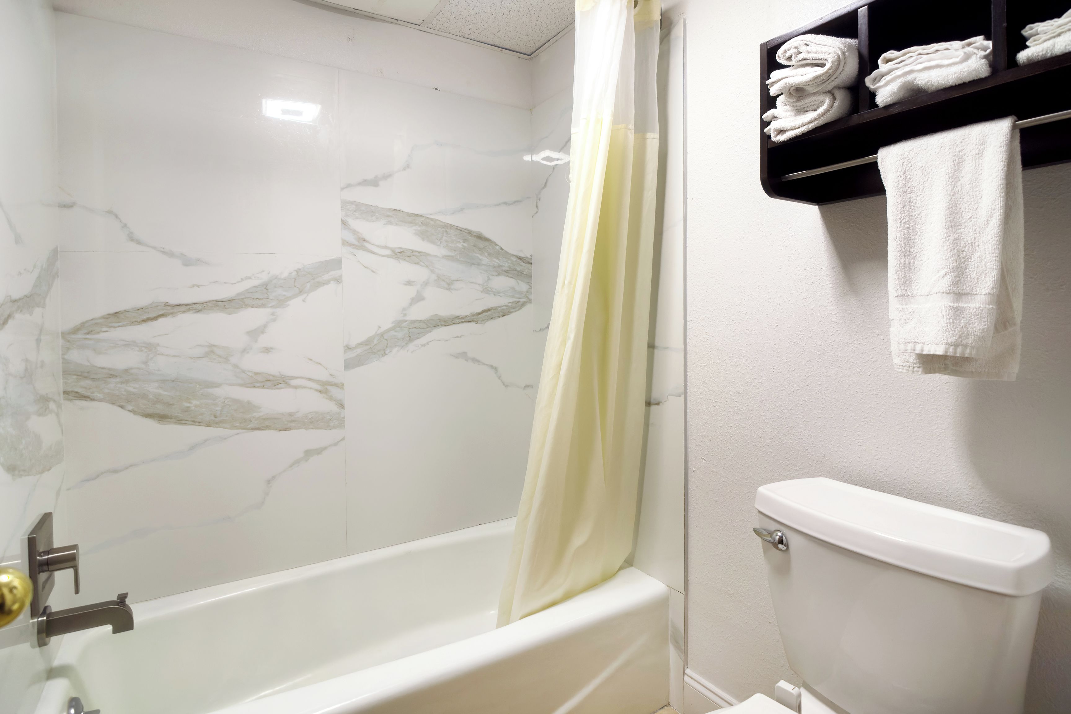 A bathroom with a bathtub, a toilet, and a towel rack with folded towels.