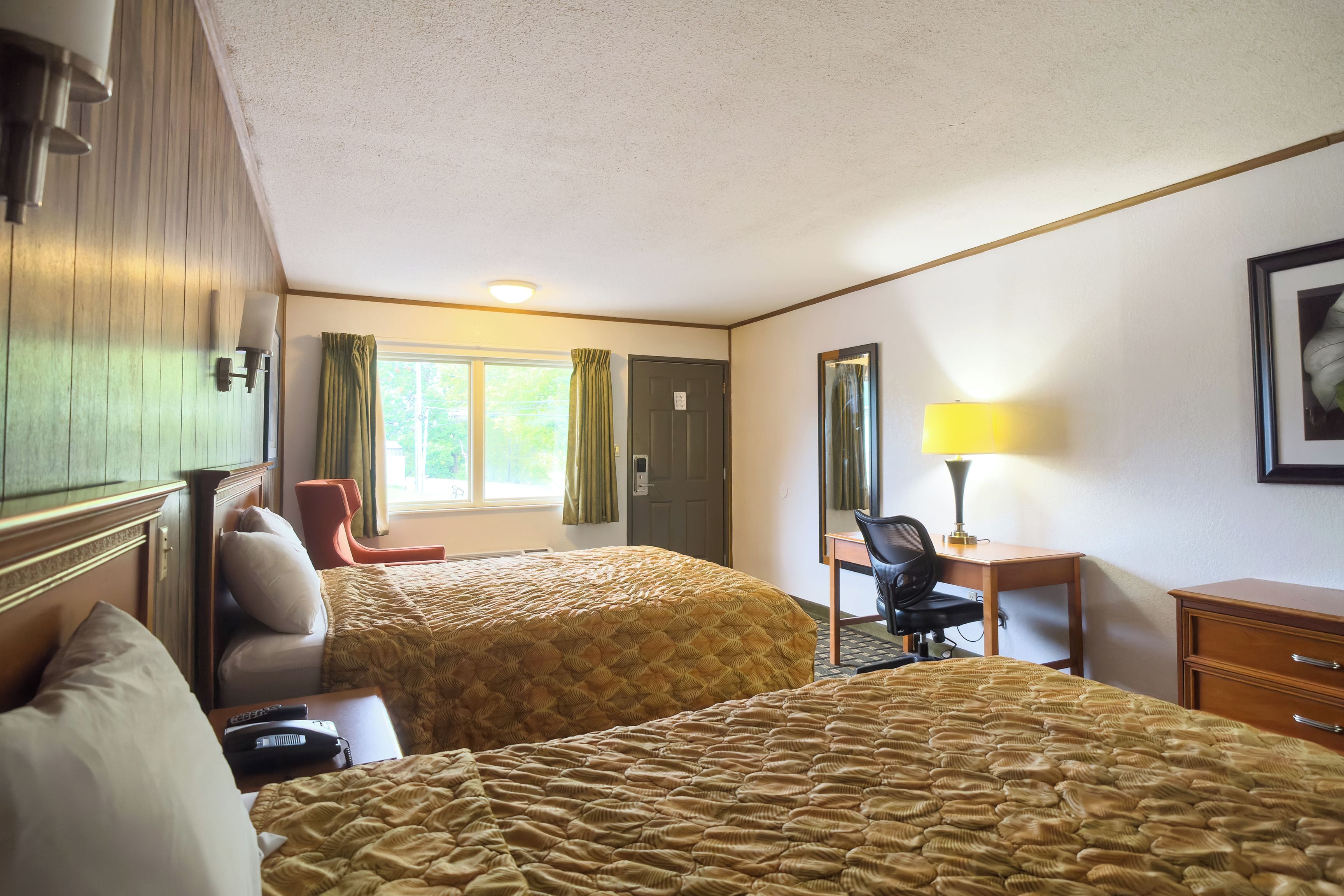 A hotel room with two beds, a desk, a chair, a lamp, and a mirror.