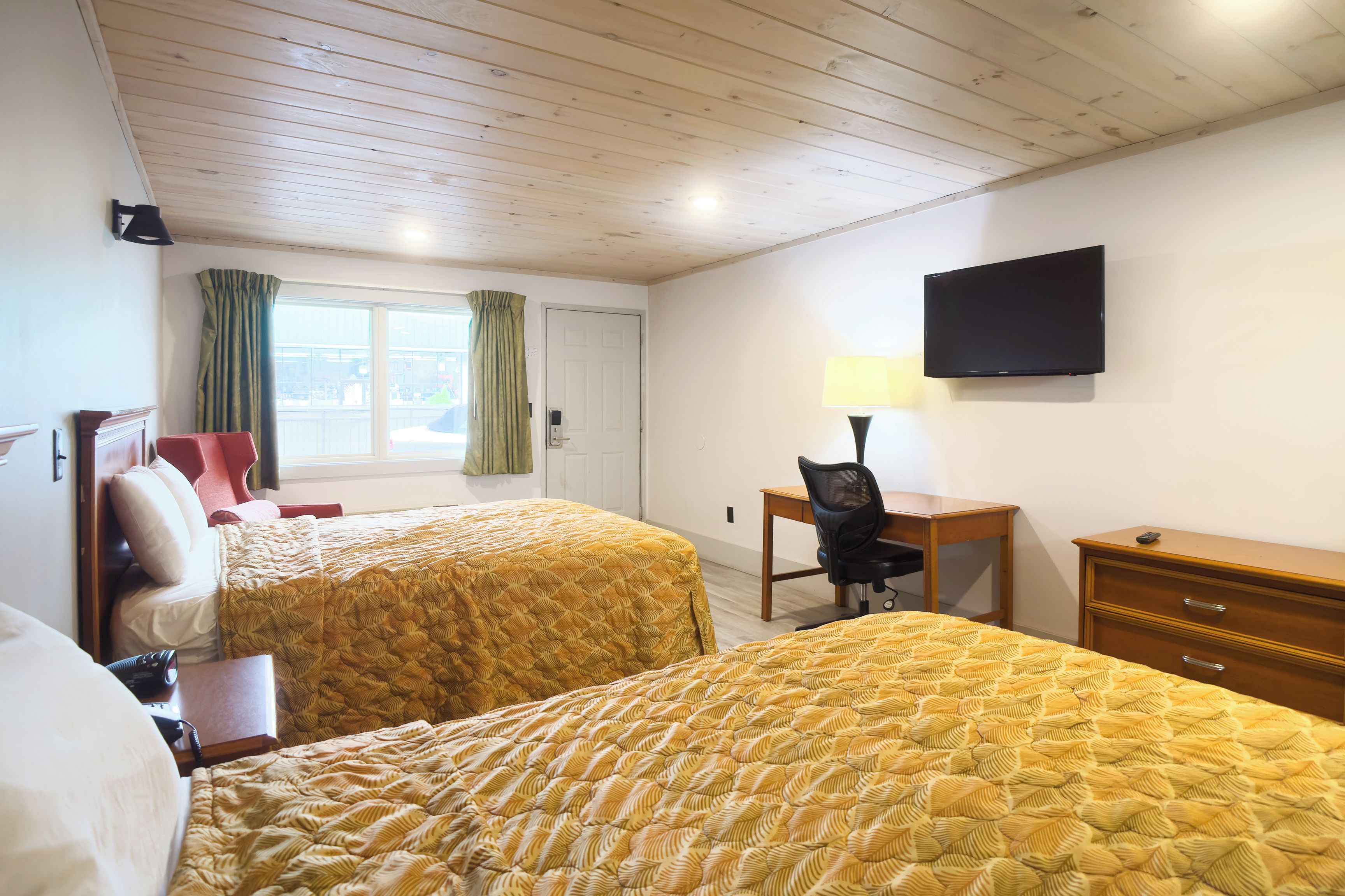 Quarto de hotel com duas camas, uma escrivaninha com cadeira, televisão e janela com cortinas.