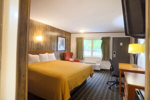 Una habitación de hotel con cama, escritorio, silla, televisor y ventana con cortinas.