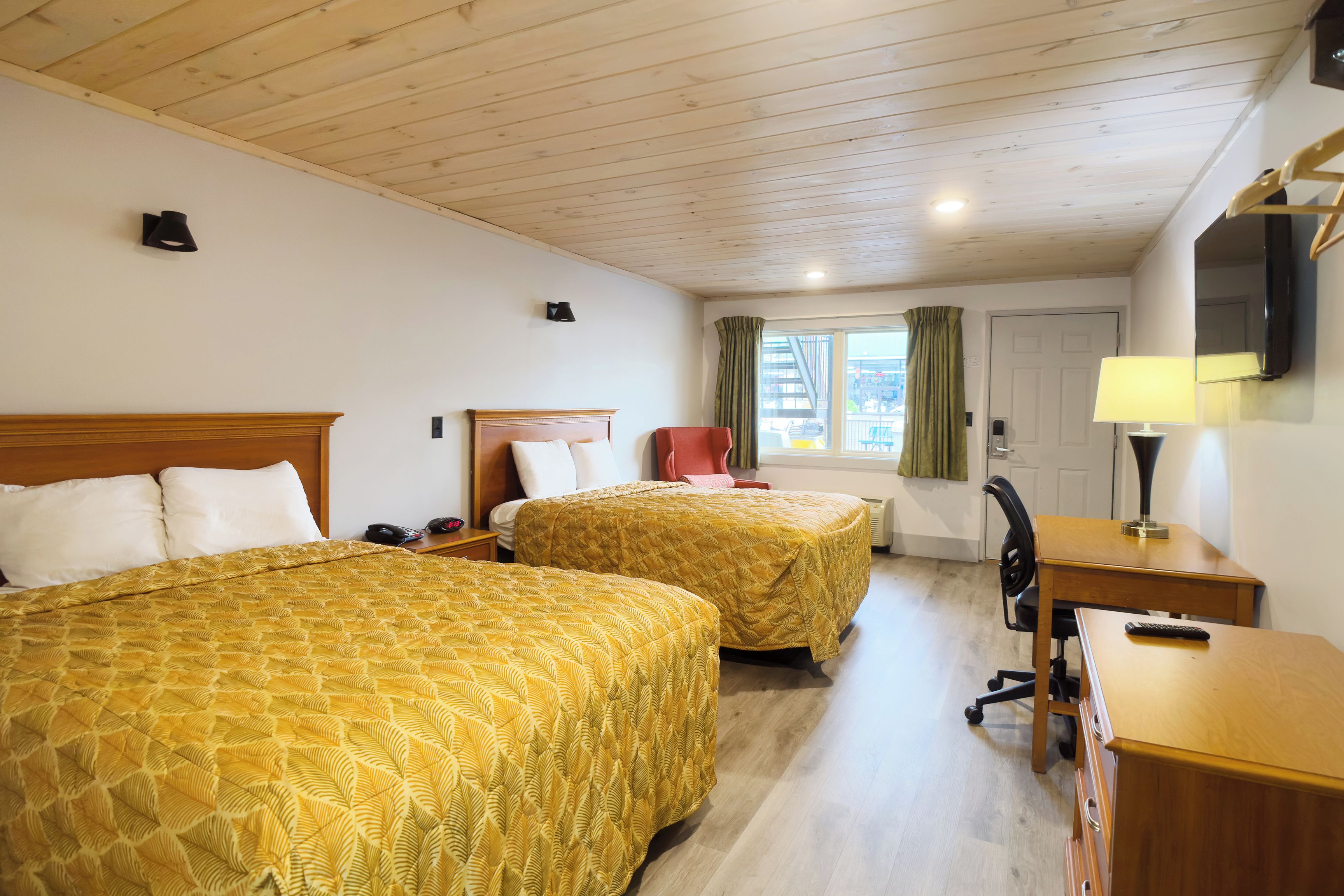 Habitación de hotel con dos camas, un escritorio, una silla, un televisor y una ventana con cortinas.