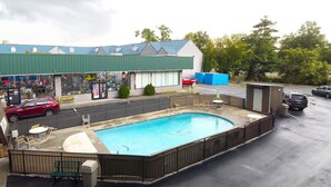 A swimming pool with a fenced deck, surrounded by a building with a green roof and a storefront.