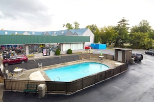 A swimming pool with a fenced deck, surrounded by a building with a green roof and a storefront.