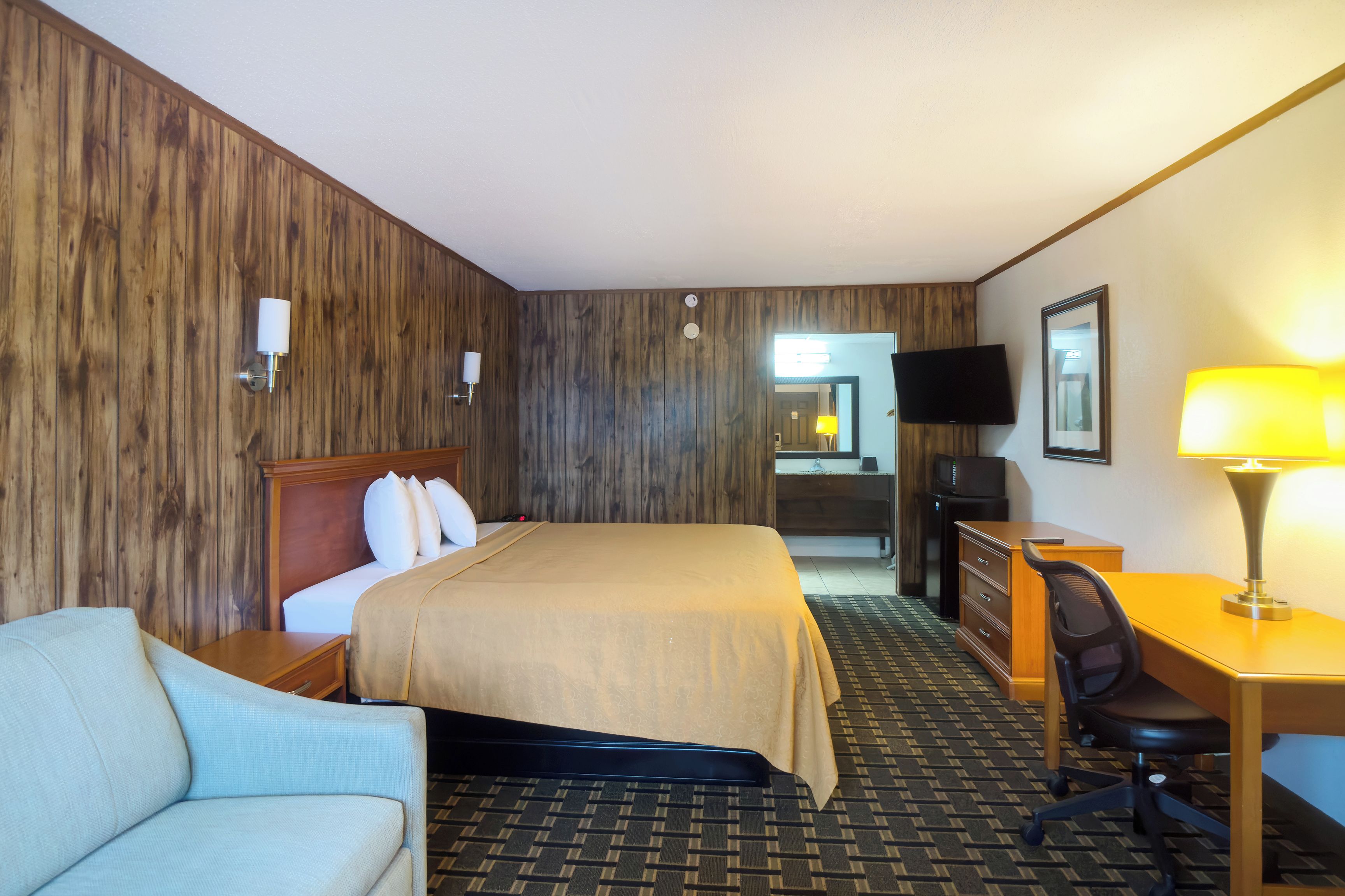 Une chambre d’hôtel équipée d’un lit, d’un bureau, d’une chaise, d’une télévision et d’une lampe de bureau.