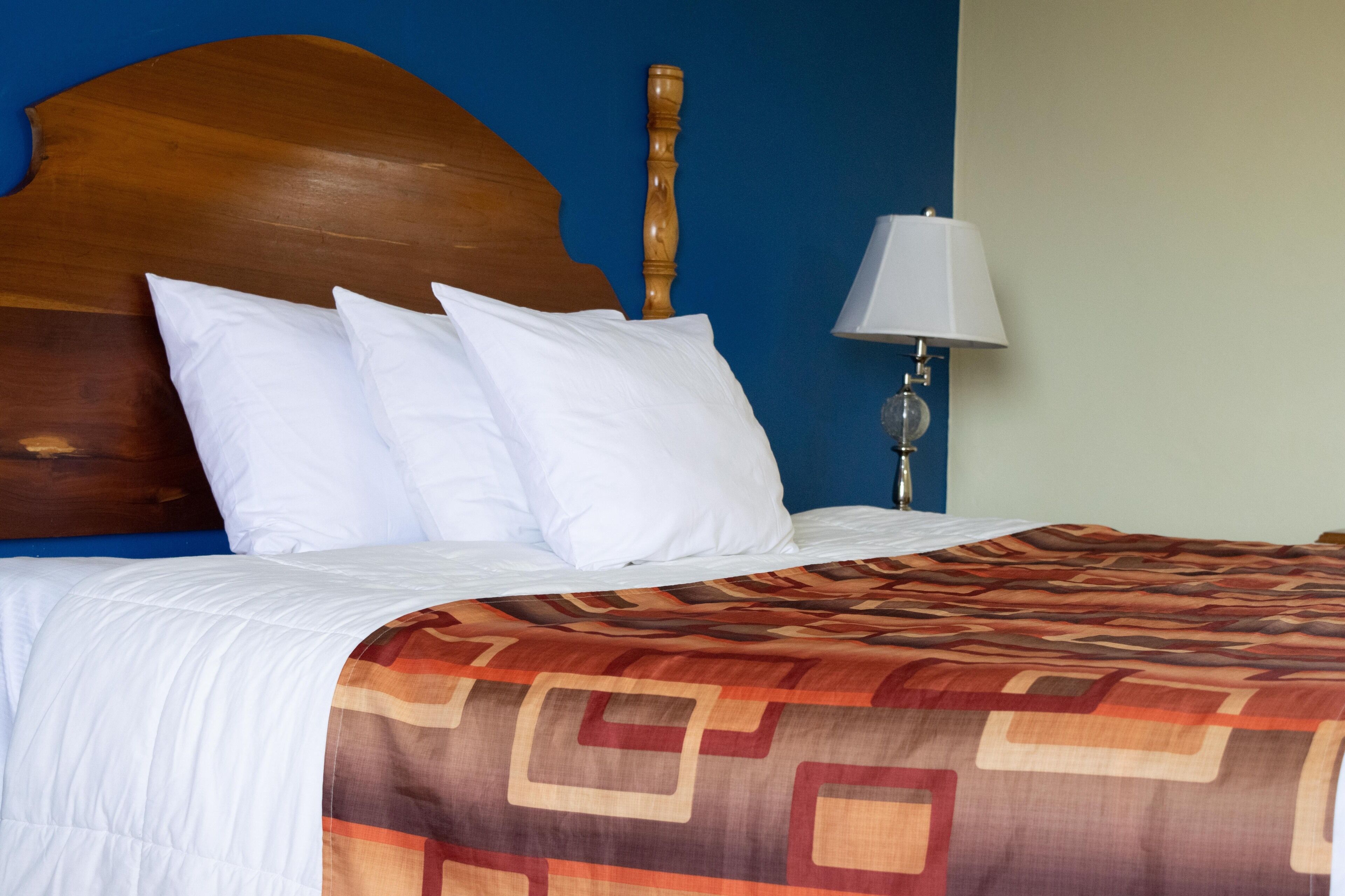 Un lit bien fait, avec des draps blancs et une couverture à motifs, une tête de lit en bois et une lampe de chevet.
