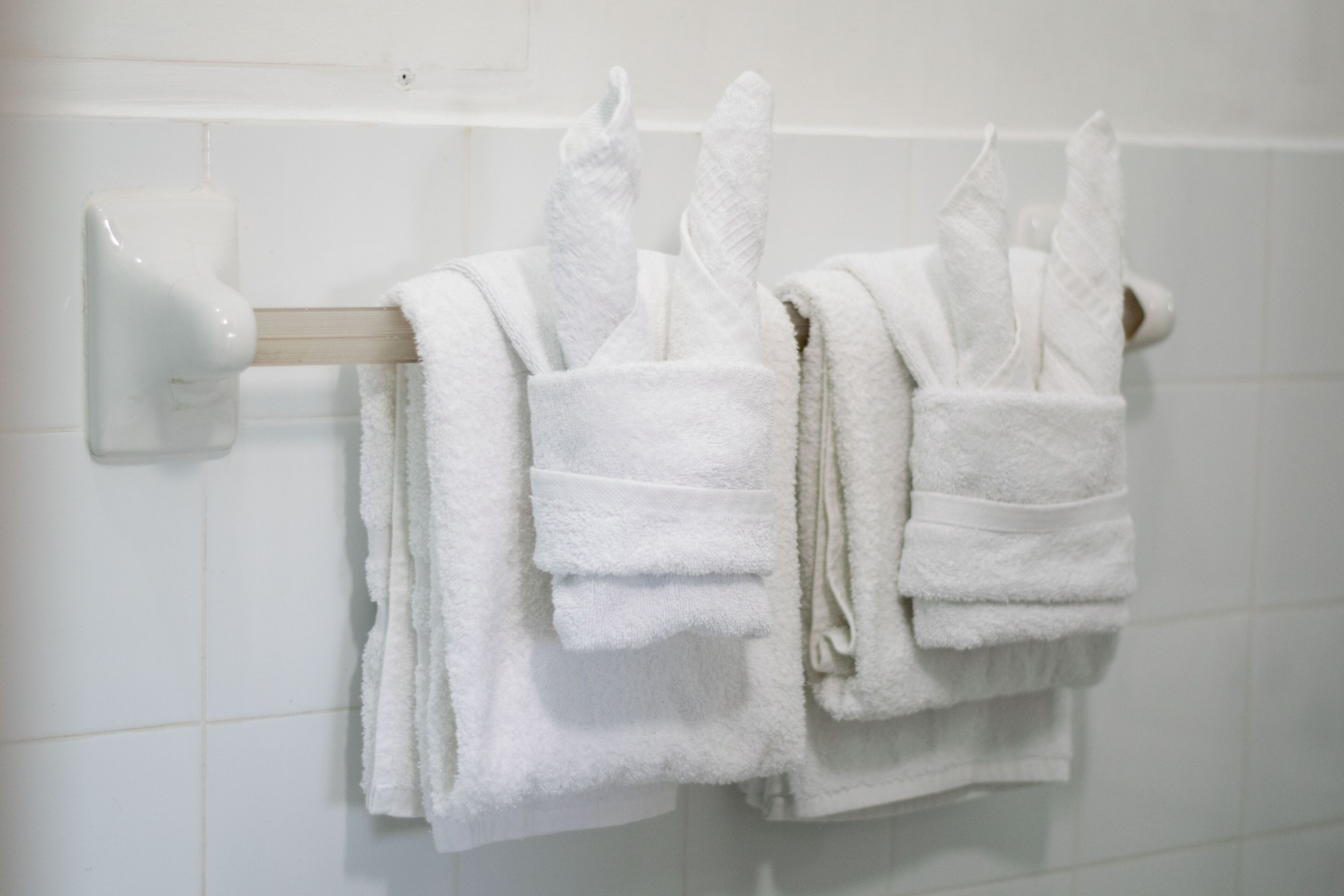 A bathroom with white tiled walls and a towel rack holding several folded white towels.