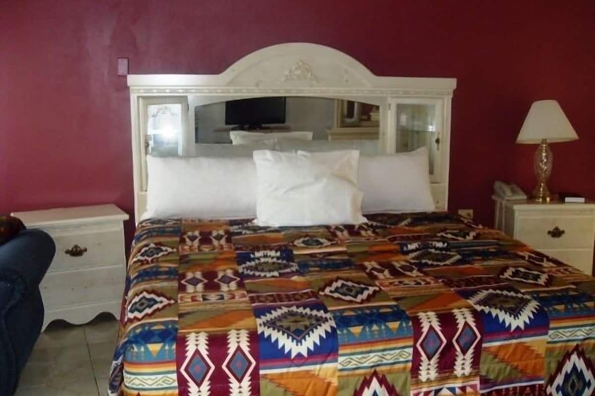 Uma cama com colcha estampada, cabeceira branca, luminária de cabeceira e mesa de apoio com um telefone.