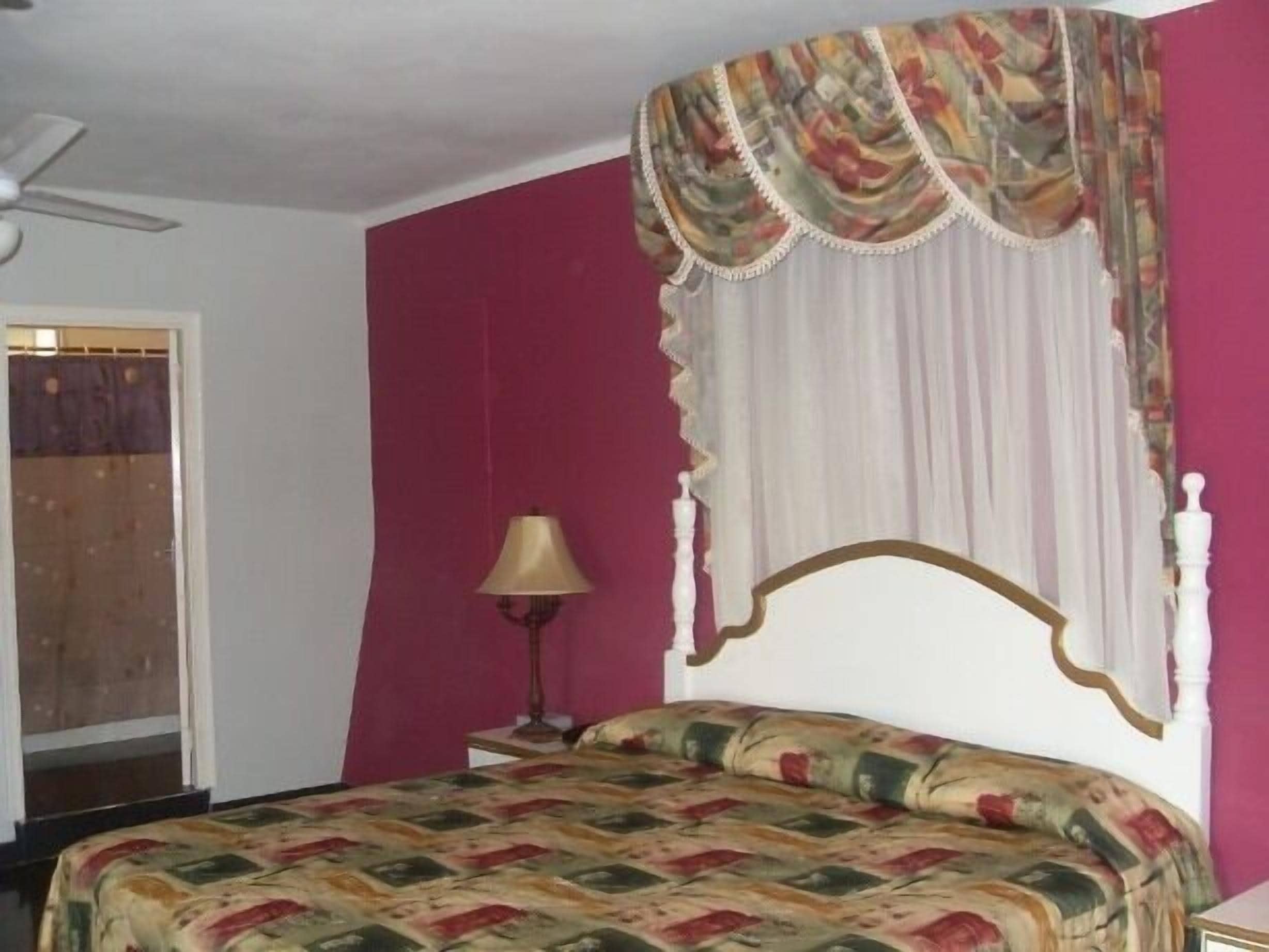 A bedroom with a bed, a ceiling fan, a lamp, and a window with curtains.