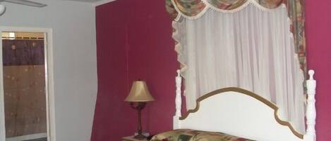 Un dormitorio con cama, ventilador de techo, lámpara y ventana con cortinas.