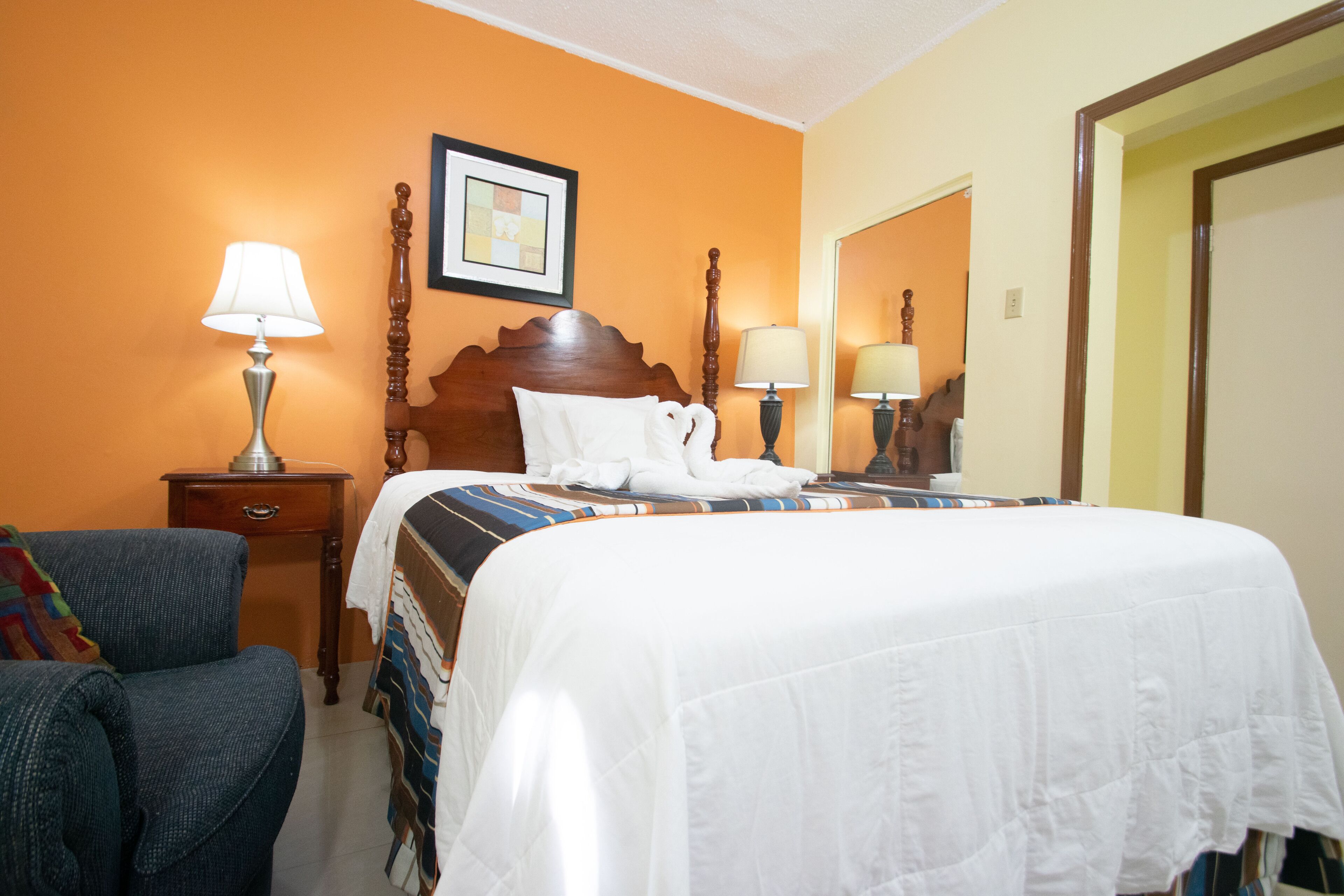 A hotel room with a large bed, two bedside tables with lamps, a chair, and a framed picture on the wall.