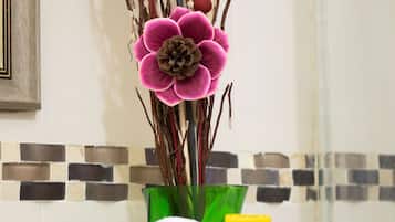 Une salle de bain avec un mur recouvert de carreaux, un vase vert contenant des fleurs roses et des serviettes blanches soigneusement pliées.