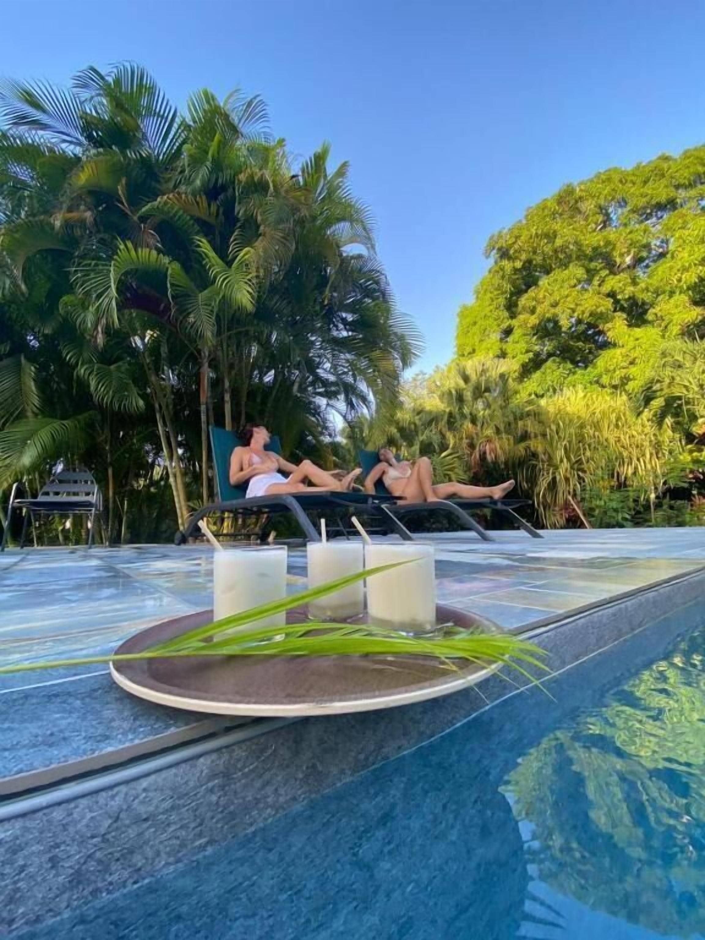 Zona junto a la piscina con sillones de descanso y una mesa con bebidas.