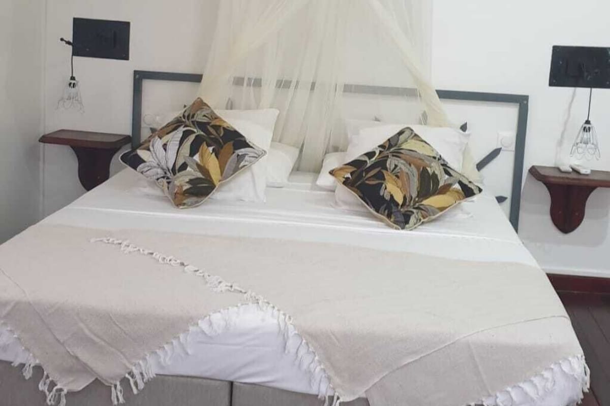 A bedroom with a canopy bed, white bedding, and two nightstands with lamps.