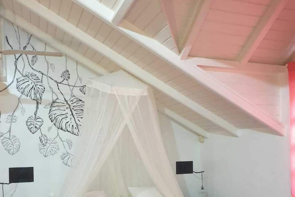 A bedroom with a bed, a canopy, a wall with leaf patterns, bedside tables, and a wooden floor.