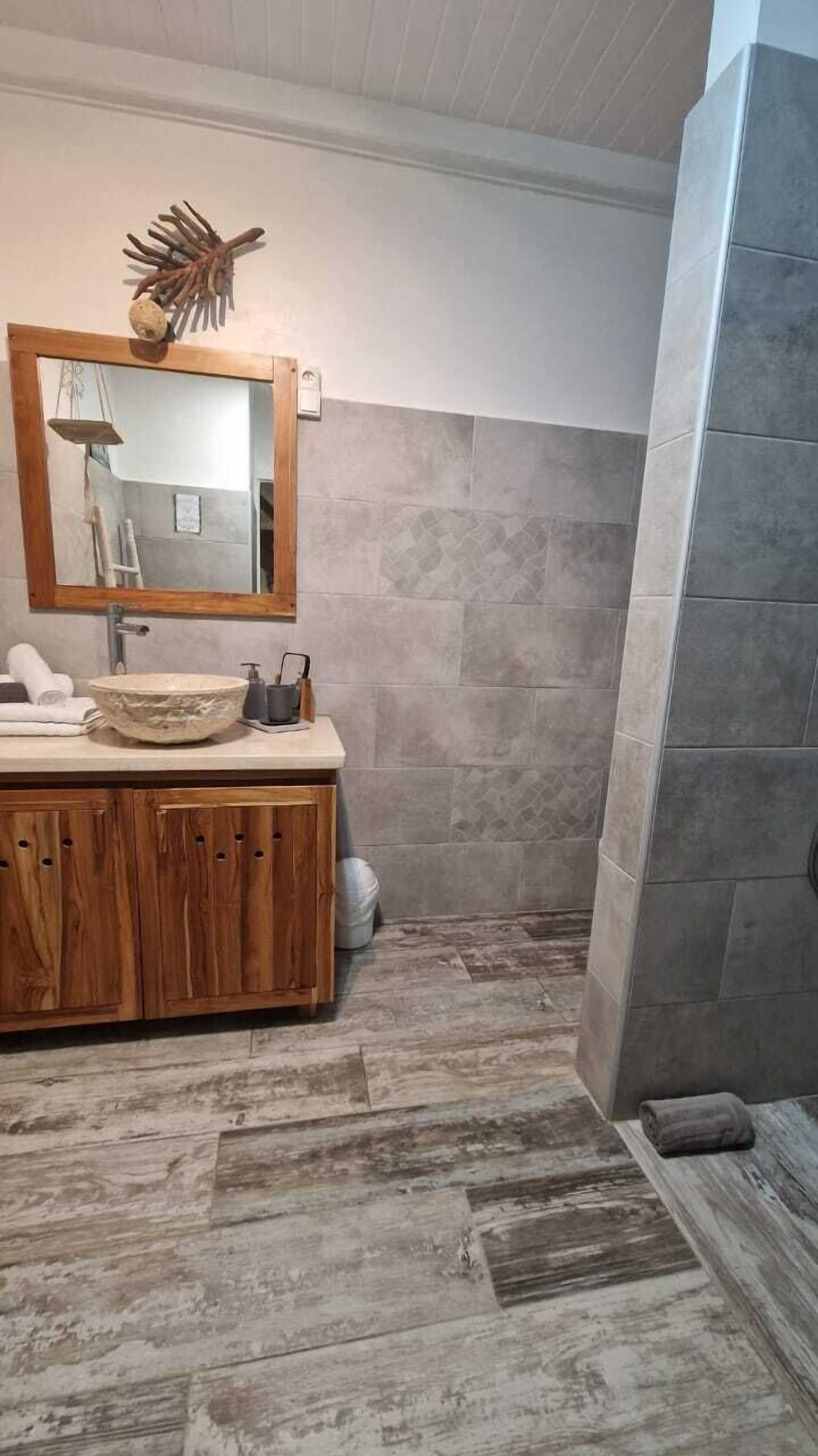 A bathroom with a wooden vanity, a large mirror, and a stone-tiled shower area.
