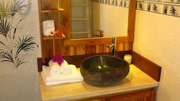 A bathroom with a wooden vanity, a large mirror, a stone basin, and a towel rack with towels.