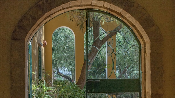 Una porta arquejada amb una reixa de metall que dona a un pati amb rajoles i vistes a arbres.
