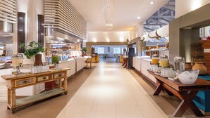 Eine großzügige Hotelhalle mit einer zentralen offenen Fläche, mehreren Buffetbereichen und einem modernen Design mit Holzakzenten und großen Fenstern.