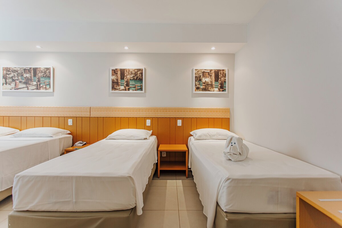 A hotel room with two beds, a wooden headboard, a small table, and three framed pictures on the wall.