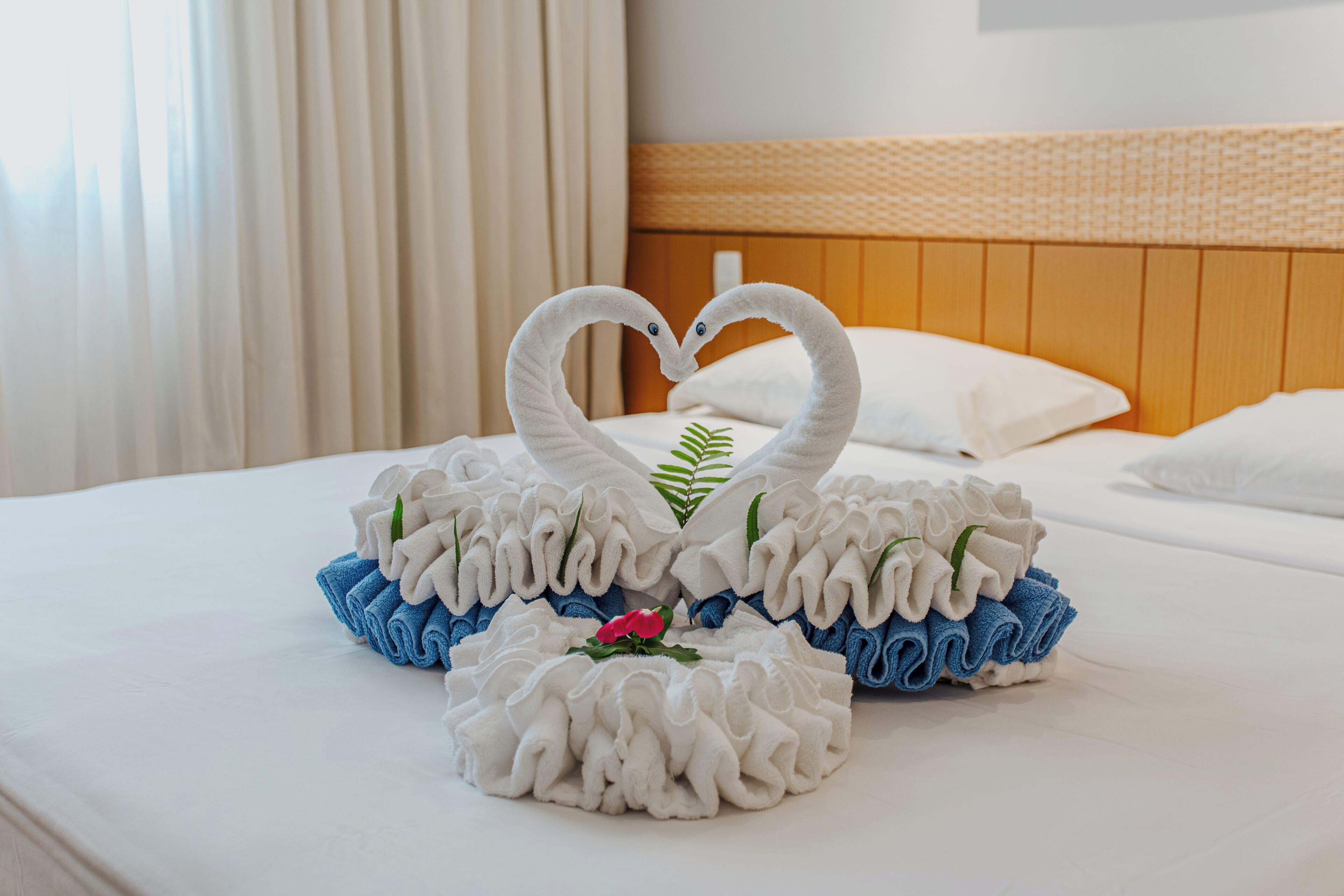 Ein ordentlich bezogenes Bett mit einer herzförmigen Handtuch-Anordnung und einer einzelnen Blume.