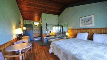 A hotel room with a wooden ceiling, a large bed, a sitting area with a table and chairs, a bathroom with a bathtub, and a mirror.