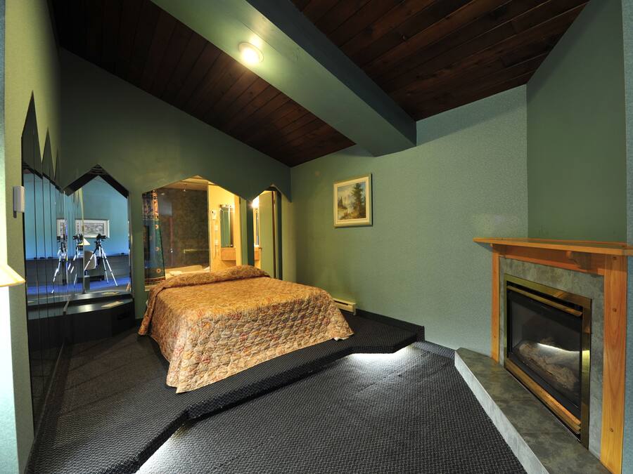 A bedroom with a bed, a fireplace, a mirror, and a ceiling with wooden beams.